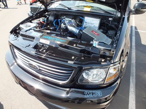 2003 Ford Crown Victoria - Close view into a black pickup's engine bay showing a supercharger and blue intake tubes, with '2973' on the bumper.