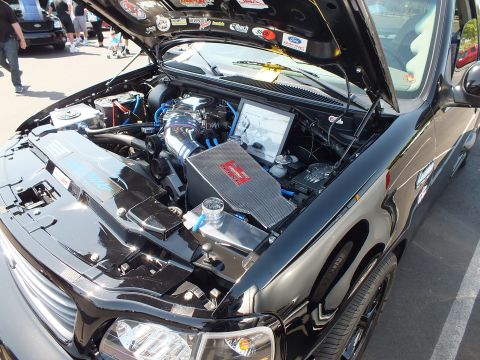 2003 Ford Crown Victoria - black truck's open engine bay featuring a supercharger, blue hoses and a perforated metal heat shield.