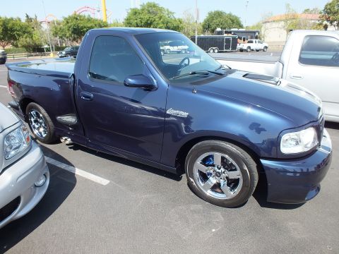 2003 Ford Crown Victoria - dark blue Ford SVT Lightning single-cab pickup with polished chrome wheels parked on car-show asphalt.