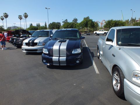 2003 Ford Crown Victoria - Front view of a dark blue Ford pickup with silver racing stripes parked among other trucks at an outdoor show.