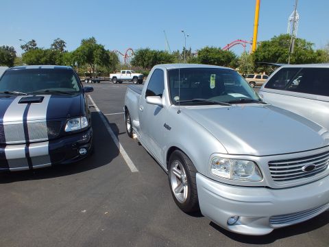 2003 Ford Crown Victoria - black pickup with silver stripes parked next to a silver Ford Lightning single-cab pickup at an outdoor show.