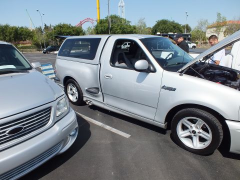 2003 Ford Crown Victoria - silver Ford pickup fitted with a bed cap and hood raised, parked beside other trucks at an outdoor car show.