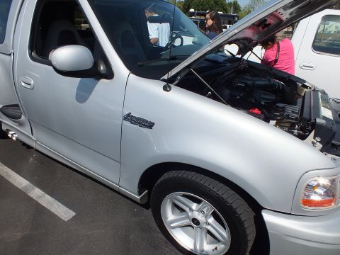 2003 Ford Crown Victoria - side of a silver Ford Lightning single-cab pickup with its hood raised and onlookers behind at a car show.