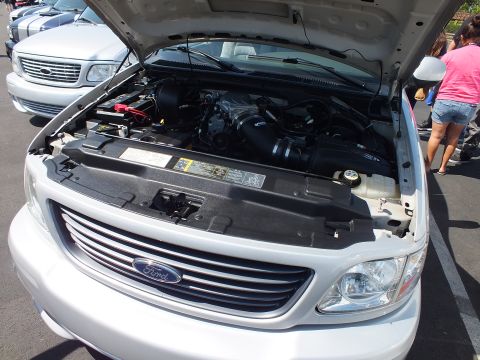 2003 Ford Crown Victoria - white Ford pickup with its hood raised, showing the engine bay and a Ford oval on the billet grille.