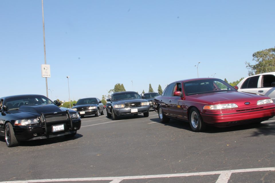 Red 1992 Ford Crown Victoria parked in a lot, front 3/4 view. Modified hood and grille on black police car in foreground