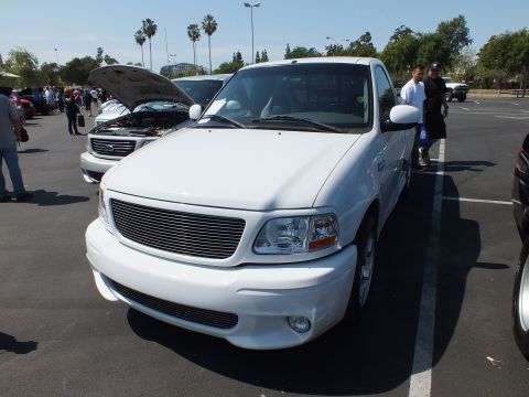 2003 Ford Crown Victoria - Front three-quarter view of a white Ford pickup with a billet grille parked among trucks at an outdoor car show.