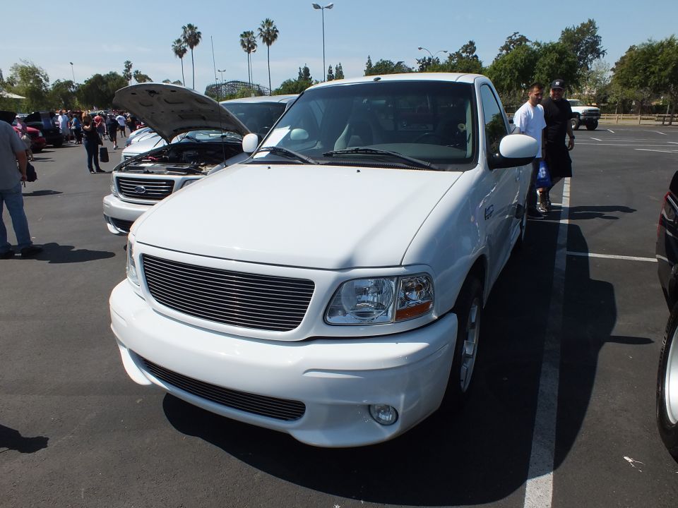 Front three-quarter of a white Ford pickup with billet grille parked at a car show