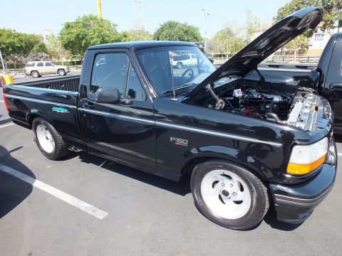 2003 Ford Crown Victoria - black Ford F-150 Lightning regular-cab pickup parked at an outdoor show with its hood raised over the engine bay.