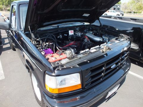 2003 Ford Crown Victoria - engine bay of a black Ford pickup with the hood open, showing a red intake plenum, alternator and battery, marked with a 95 placard.