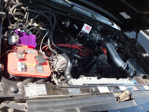 2003 Ford Crown Victoria - close-up of an engine bay showing a red battery, purple ignition coil, serpentine belt and alternator under an open hood.