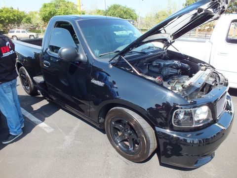 2003 Ford Crown Victoria - lowered black Ford F-150 Lightning regular-cab pickup with its hood raised, sitting on black wheels at a car show.