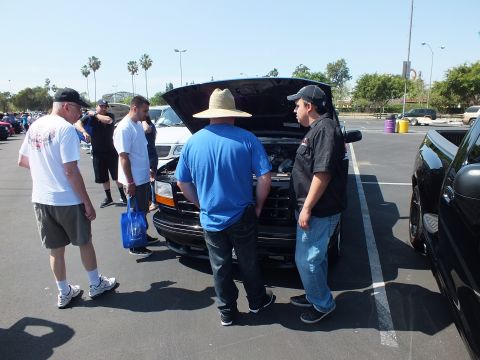 2003 Ford Crown Victoria - Several men in casual clothing gather around a dark Ford pickup with its hood open in a sunny parking-lot car show.