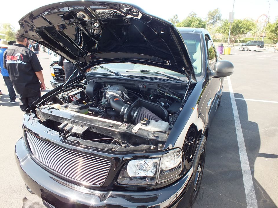 Black Ford F-150 pickup with hood open showing billet grille and engine bay