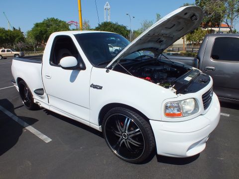 2003 Ford Crown Victoria - white Ford F-150 Lightning regular-cab pickup with hood raised, lowered on black-lipped chrome wheels at a car show.