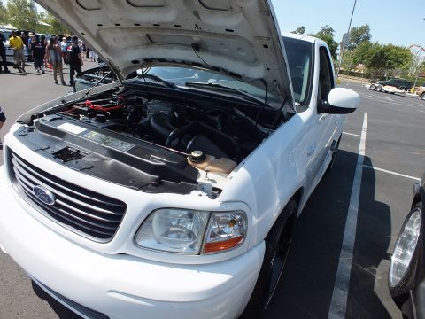 2003 Ford Crown Victoria - white Ford F-150 pickup shot from the upper front with its hood open, revealing the engine bay at an outdoor car show.