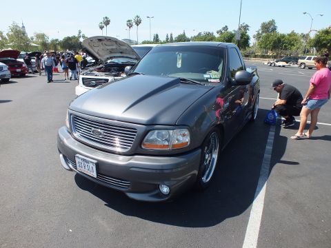 2003 Ford Crown Victoria - front three-quarter view of a charcoal Ford F-150 Lightning pickup with a billet grille and front plate at a packed car show.