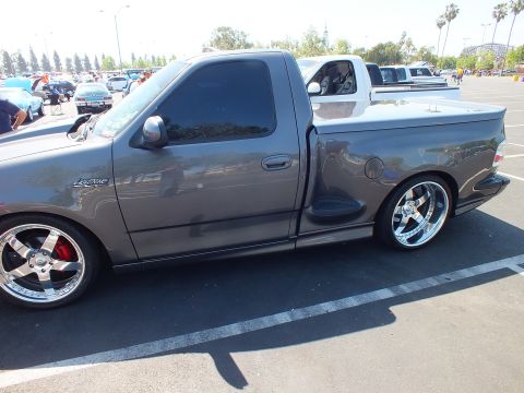 2003 Ford Crown Victoria - side profile of a charcoal Ford F-150 Lightning regular-cab pickup, lowered on chrome wheels with red calipers, at a show.