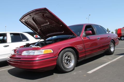 1992 Ford Crown Victoria - A red 1992 Ford Crown Victoria is parked with its hood up, revealing engine work and custom wheels.
