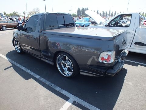 2003 Ford Crown Victoria - rear three-quarter view of a charcoal Ford F-150 Lightning pickup, lowered on chrome wheels, parked among show cars.