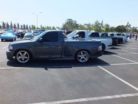 2003 Ford Crown Victoria - side profile of a charcoal Ford F-150 Lightning regular-cab pickup, lowered on polished chrome wheels, at an outdoor show.