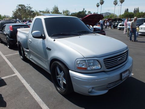 2003 Ford Crown Victoria - front three-quarter view of a silver Ford F-150 Lightning pickup with a billet grille, parked at a crowded car show.