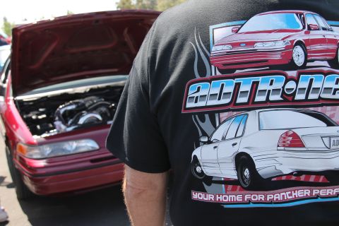 1992 Ford Crown Victoria - A red sedan's engine is visible with its hood up, while a person in a graphic t-shirt stands in front.