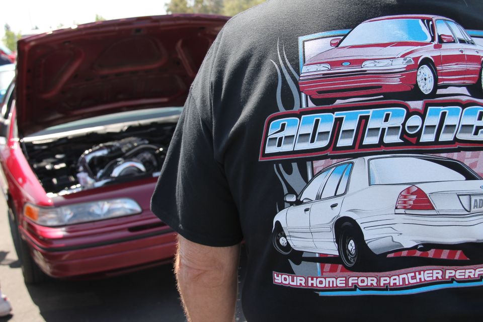 Red sedan with hood open, showing engine. Person in foreground wears shirt with graphics of red and white sedans