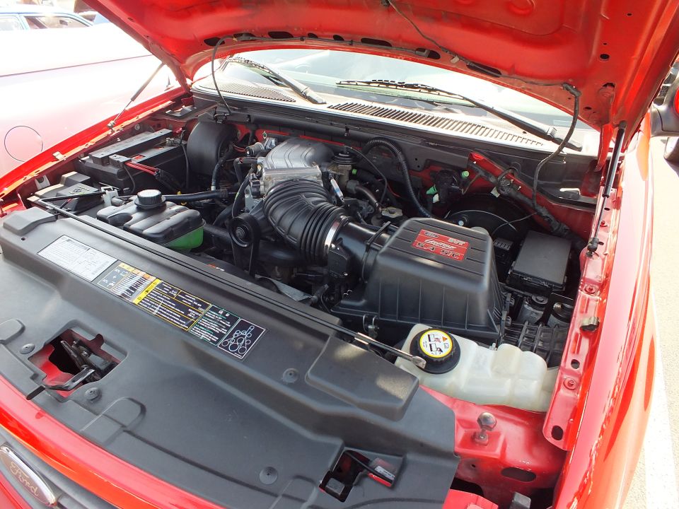 Engine bay of a red Ford truck showing a supercharger intake assembly