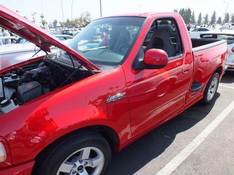 2003 Ford Crown Victoria - red Ford F-150 Lightning regular-cab pickup with its hood raised, parked on the lot at a large outdoor car show.