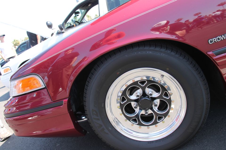 Close-up of a red sedan's front fender and wheel. Text on the side says CROWN