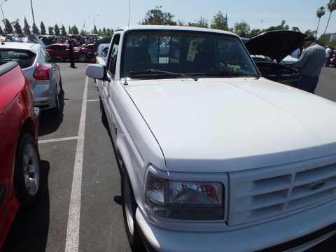 2003 Ford Crown Victoria - white Ford F-150 pickup shot from the front and above, with its hood open, among many cars at a crowded outdoor show.