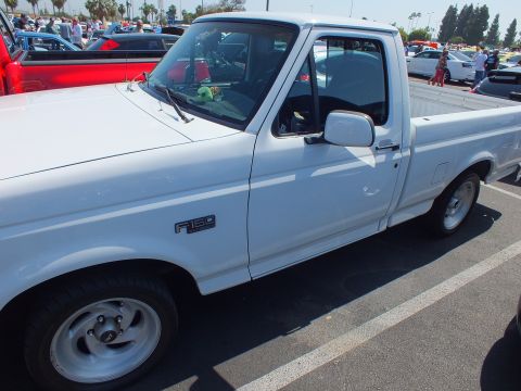 2003 Ford Crown Victoria - Side view of a white 1990s Ford F-150 single-cab pickup parked at an outdoor car show.