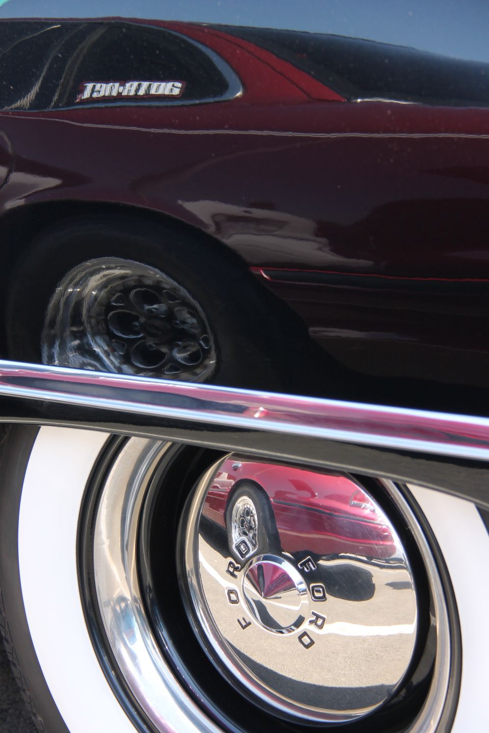 Reflection of a red car on the hubcap of a 1992 Ford Crown Victoria. The car has whitewall tires