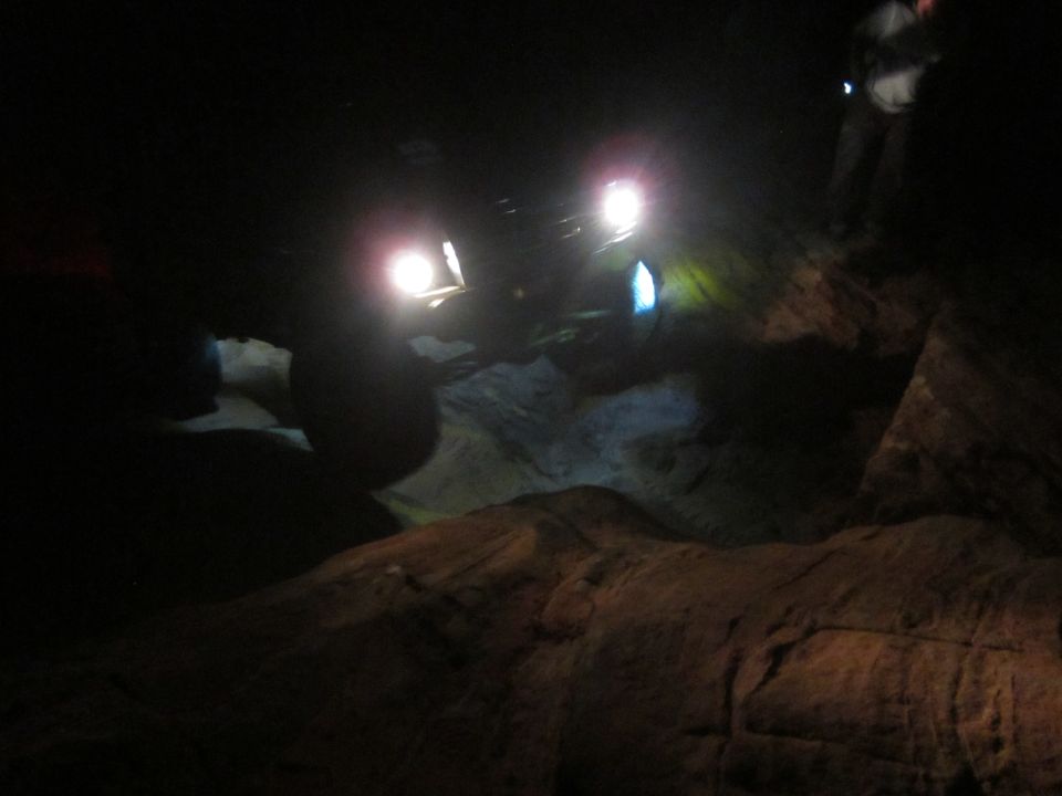 Dark scene with two off-road vehicles with bright headlights on rocky terrain