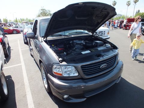 2003 Ford Crown Victoria - Gray Ford pickup with its hood raised displaying the engine, parked at a crowded outdoor car show.