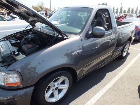 2003 Ford Crown Victoria - Side three-quarter view of a gray Ford SVT Lightning pickup with raised hood at a car show.