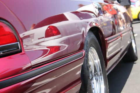 1992 Ford Crown Victoria - A close-up side view of a red 1992 Ford Crown Victoria, highlighting its chrome wheels and the reflections on its polished surface.