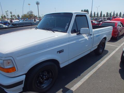 2003 Ford Crown Victoria - Side view of a white 1990s Ford F-150 single-cab pickup with black steel wheels at a car show.
