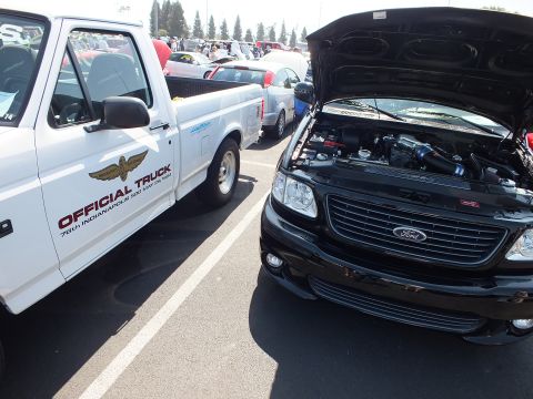 2003 Ford Crown Victoria - white 75th Indianapolis 500 official pickup parked beside a black Ford Lightning with its hood up.