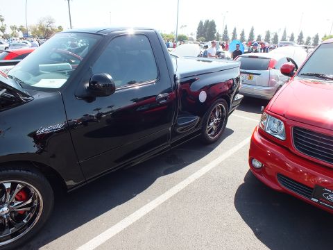 2003 Ford Crown Victoria - Black Ford Lightning pickup with chrome wheels parked beside a red Ford pickup at a car show.