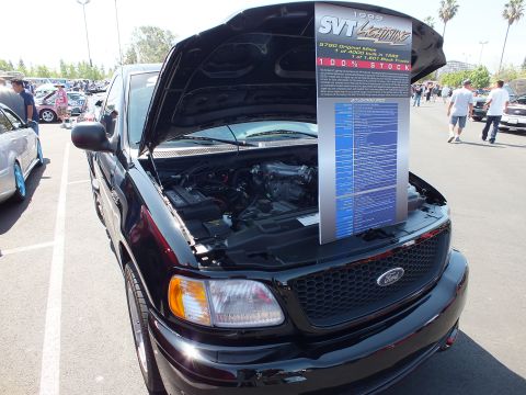 2003 Ford Crown Victoria - Black Ford SVT Lightning displayed with hood open and a printed information placard at a car show.