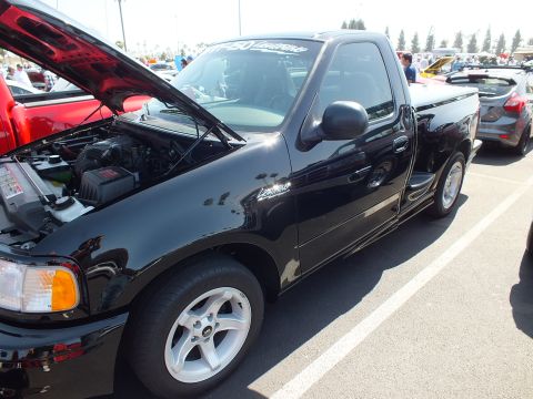 2003 Ford Crown Victoria - Side three-quarter view of a black Ford F-150 Lightning pickup with hood raised at a car show.