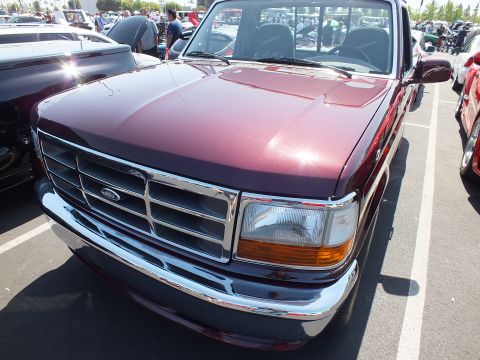 2003 Ford Crown Victoria - Close front three-quarter view of a maroon Ford F-150 pickup showing its chrome grille and oval emblem.