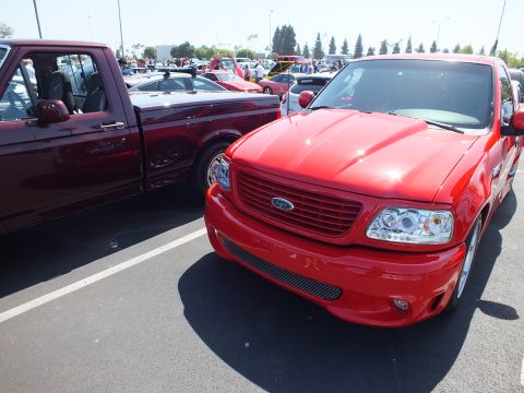 2003 Ford Crown Victoria - Front end of a red Ford F-150 Lightning pickup parked beside another dark red pickup at a car show.