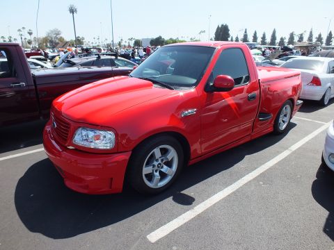 2003 Ford Crown Victoria - Side three-quarter view of a red Ford F-150 Lightning pickup with alloy wheels at an outdoor car show.
