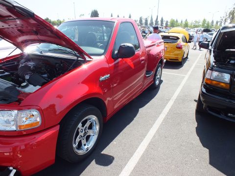 2003 Ford Crown Victoria - red Ford F-150 Lightning sport truck sits with its hood raised among other show vehicles in a sunny parking lot.