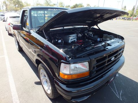 2003 Ford Crown Victoria - black Ford F-150 Lightning pickup displays its supercharged engine bay with the hood open in a parking lot show.