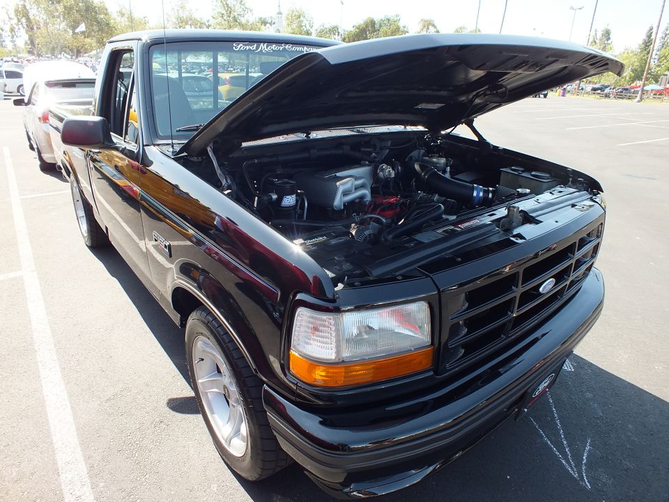 Black Ford F-150 Lightning pickup with hood up showing supercharged engine at car show