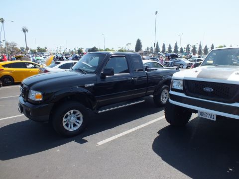 2003 Ford Crown Victoria - black Ford Ranger extended-cab pickup sits next to a white lifted Ford truck in a packed car-show parking lot.