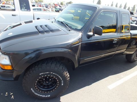 2003 Ford Crown Victoria - black Ford Ranger extended cab on BFGoodrich Mud-Terrain tires and black wheels parks at a sunny outdoor car meet.